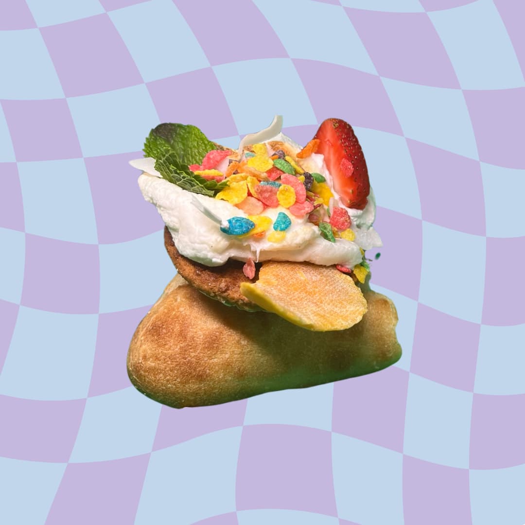 A s'more topped with whipped cream, cereal, mint and a strawberry against a lavender checkerboard backdrop