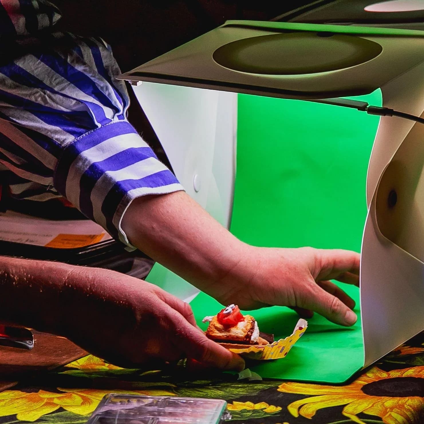 Hands placing a finished s'more inside a small photo booth with a green backdrop